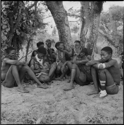 /Gunda wearing bandages, sitting with a group of people in the shade