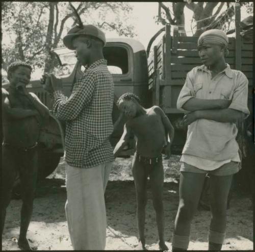 ≠Toma, Tsamgao and a boy standing with an expedition member next to a truck, talking