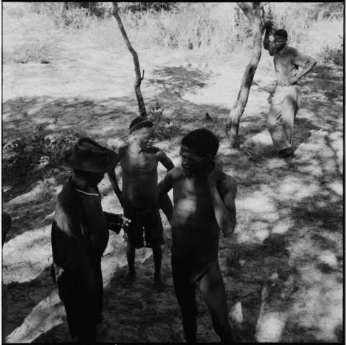 "/Gao Music" standing with two men, talking, with a man leaning against a tree in the background