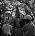 /Ti!kay standing in the back of an expedition truck, looking at two men standing next to the truck