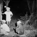 Three boys squatting and standing next to a tree at night