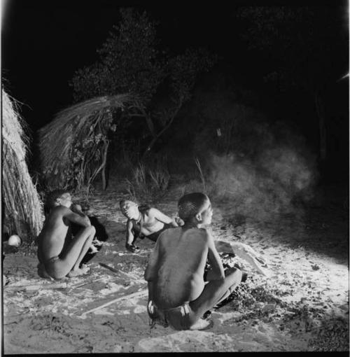 Three men sitting and lying down next to a skerm at night