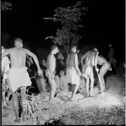 Men dancing by a group of women sitting, clapping and singing for a night dance