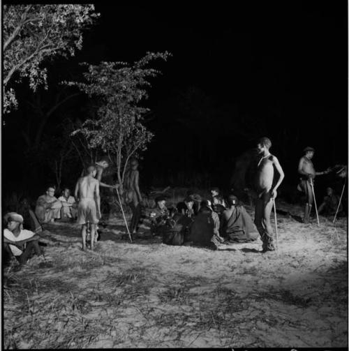 Men dancing around a group of women sitting, clapping and singing for a night dance