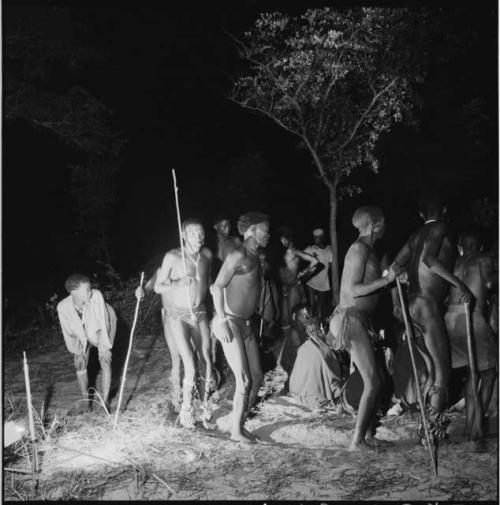 Men dancing around a group of women sitting, clapping and singing for a night dance