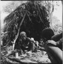 Two women sitting in front of a skerm, one handing a pipe to the other