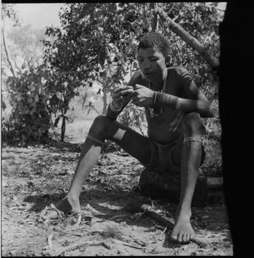 !Naishi wearing many ornaments, sitting and eating, with his foot resting on his axe