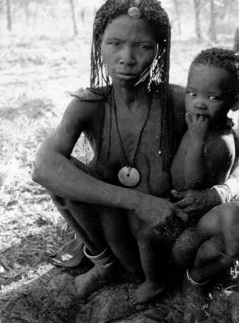 Maha r N!ame (wife of !Kalulu) sitting, holding her son, Mishi