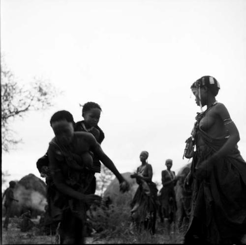 Woman playing tamah n!o’an (ball game) / !’hu kuitzi (veldkos game), holding the ball, carrying a girl on her back