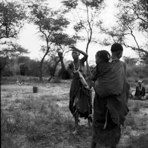 Women playing tamah n!o’an (ball game) / !’hu kuitzi (veldkos game), with one woman catching the ball, another walking by with a baby tied to her back