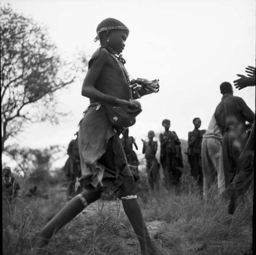 Girl playing tamah n!o’an (ball game) / !’hu kuitzi (veldkos game), walking and holding a veldkos ball, with another person's hands ready to receive it