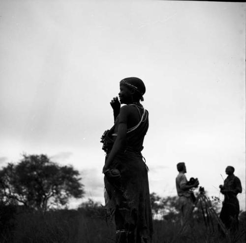 Woman playing tamah n!o’an (ball game) / !’hu kuitzi (veldkos game), with John Marshall standing in the background