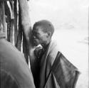 "/Gao Medicine" wearing a blanket over his shoulders, standing, leaning against a fence