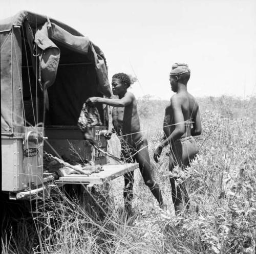 Man putting a piece of meat in the back of the expedition Jeep, with another man standing behind him