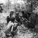 Five hunters squatting, dividing the meat from a hunt, with the expedition Jeep in the background