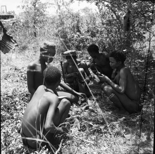 Five hunters squatting, dividing the meat from a hunt, with the expedition Jeep in the background