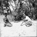 Boy sitting in the sand behind two expedition members playing /Ui (the counting game)