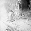 Woman sitting in front of a skerm, stirring nuts in a fire with a long stick