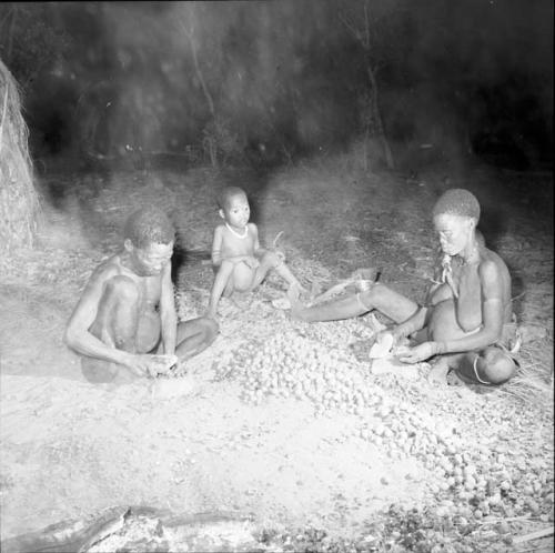 Woman and a man sitting, cracking nuts, with their child sitting behind them