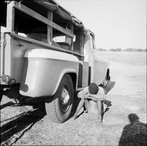 Man sitting next to an expedition truck, resting his head on his arms