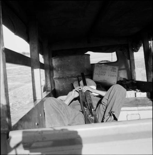 Man wearing a helmet, sleeping in the back of a truck, holding two rifles