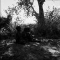 Three children sitting in the shade, clapping and singing