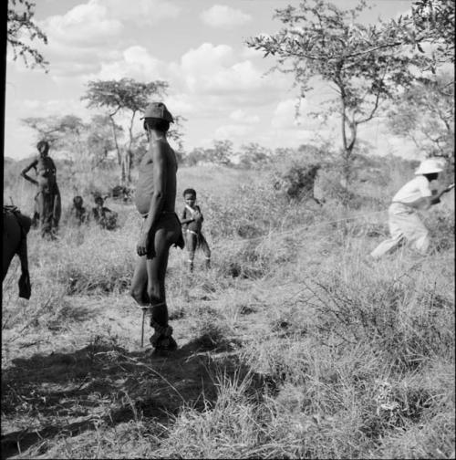 Man wearing dance rattles for a daytime dance, standing, looking at a group of people in the background