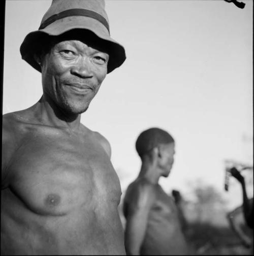 /Ti!kay wearing a hat, close-up, with another man standing behind him