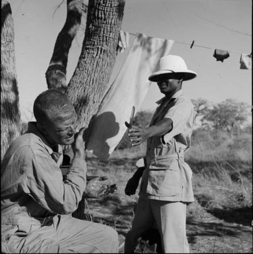 Expedition member holding a mirror for Nicholas England who is wiping "Smeermiddels" on his face