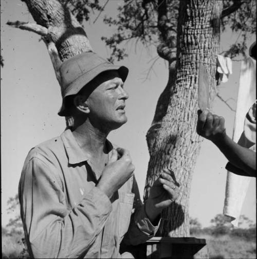 Expedition member's hand holding a mirror for Nicholas England who is wiping "Smeermiddels" on his face