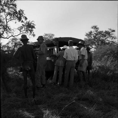 Men standing with John Marshall and other expedition members, looking in the back of the truck, view from behind