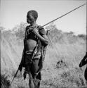 Man standing, holding an assegai, with other hunting equipment on his belt and over his shoulder