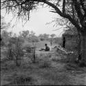 Man sitting next to a fire in front of a skerm, with a child standing near him, skerms in the background