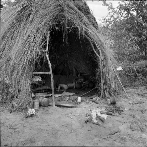 Woman and a baby sleeping inside a skerm, with possessions on the ground near the entrance