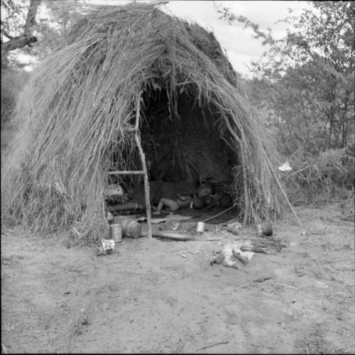 Woman and a baby sleeping inside a skerm, with possessions on the ground near the entrance