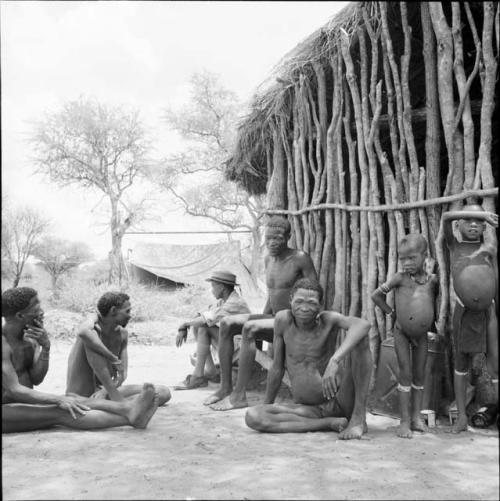 Group of men sitting outside the expedition hut, with two children standing next to them