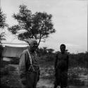 /Ti!kay standing with Laurence Marshall, with an expedition tent in the background