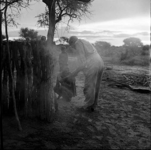 Man squatting next to the expedition hut, shaking hands with Laurence Marshall, with smoke blowing across them