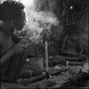 Man making a hole for his adze with a heated awl, sitting with a group of men in front of a skerm