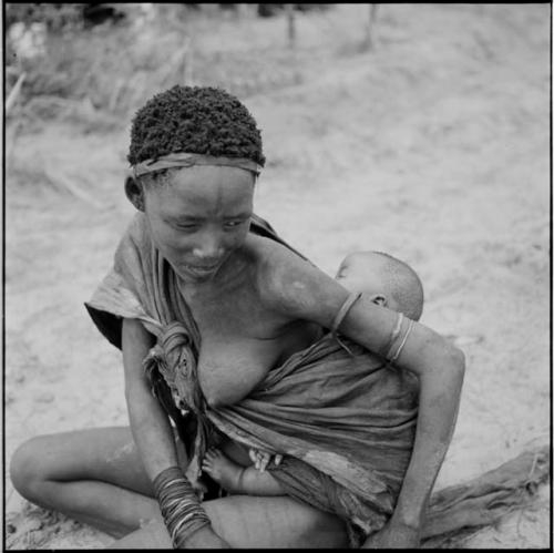 Woman sitting, with her baby tied in her kaross