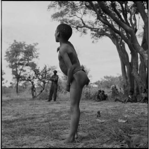 Boy standing, profile, with people sitting and standing in the background