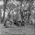 Man making a //guashi, sitting with a group of men, being photographed by Robert Gardner