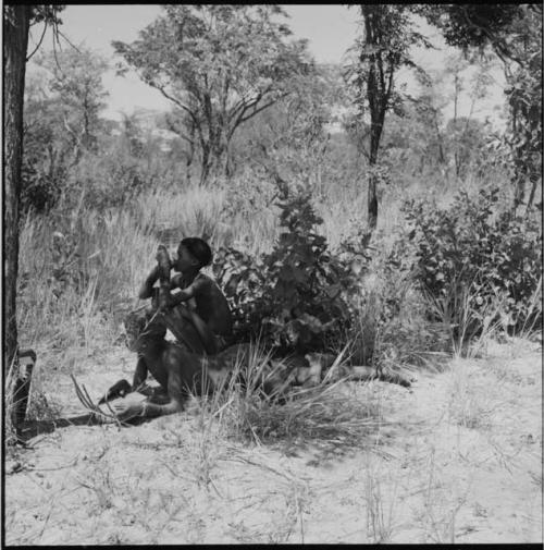 Boy smoking a pipe, with another boy lying down next to him, playing a //guashi