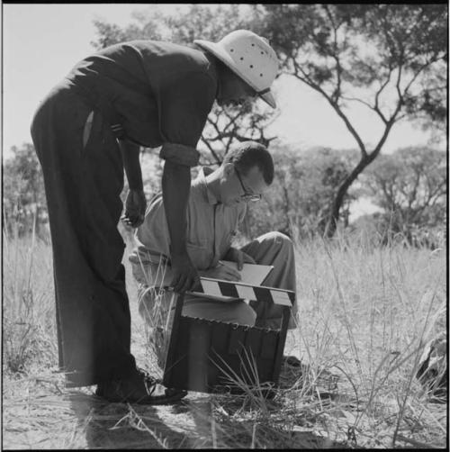 Kernel Ledimo leaning over, holding a clapstick, with Nicholas England sitting next to him, writing in a notebook