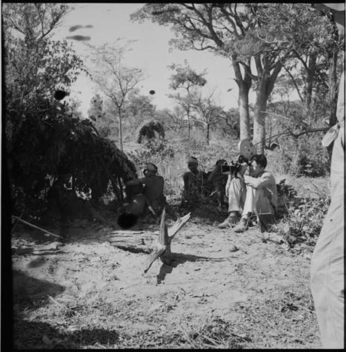 Group of women and children sitting inside and in front of a shelter skerm, with an expedition member filming them