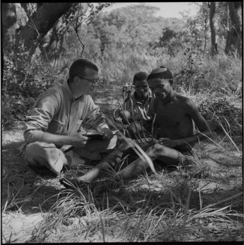 "/Gao Music" playing a //guashi and singing, with another man and Nicholas England sitting next to him, listening