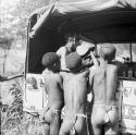 Three boys handing something to a woman sitting in the back of the expedition Jeep