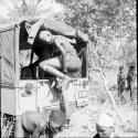 Woman climbing out of the back of the expedition Jeep, with ≠Nisa sitting behind her, three boys standing near them