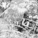 Boy squatting amongst grass and bushes