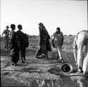 Two women standing, looking at John Marshall who is wrapped in a blanket, with other expedition members standing near them